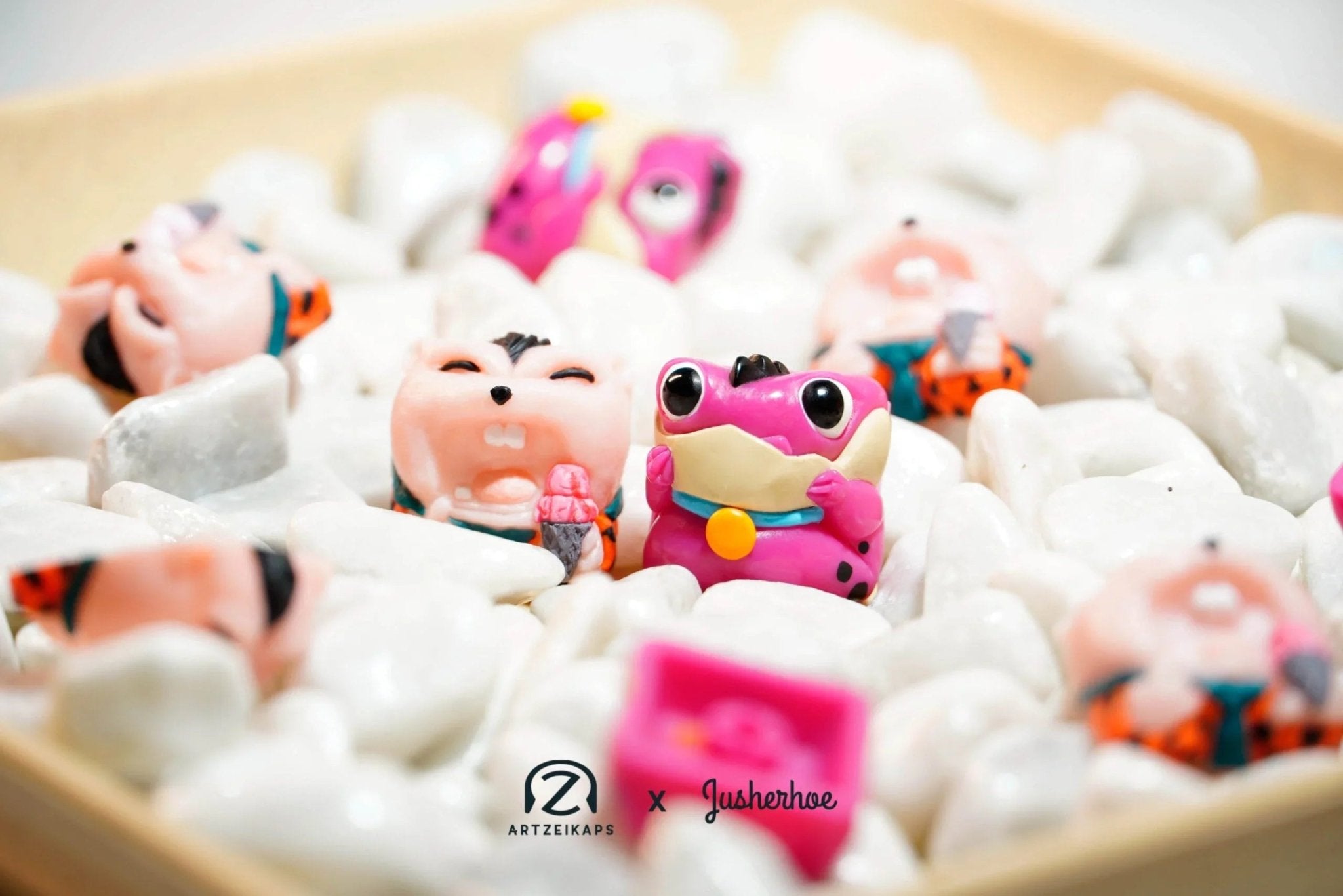 Chomper Flintstones artisan keycaps in pink and teal in a bowl of white rocks, top-down view