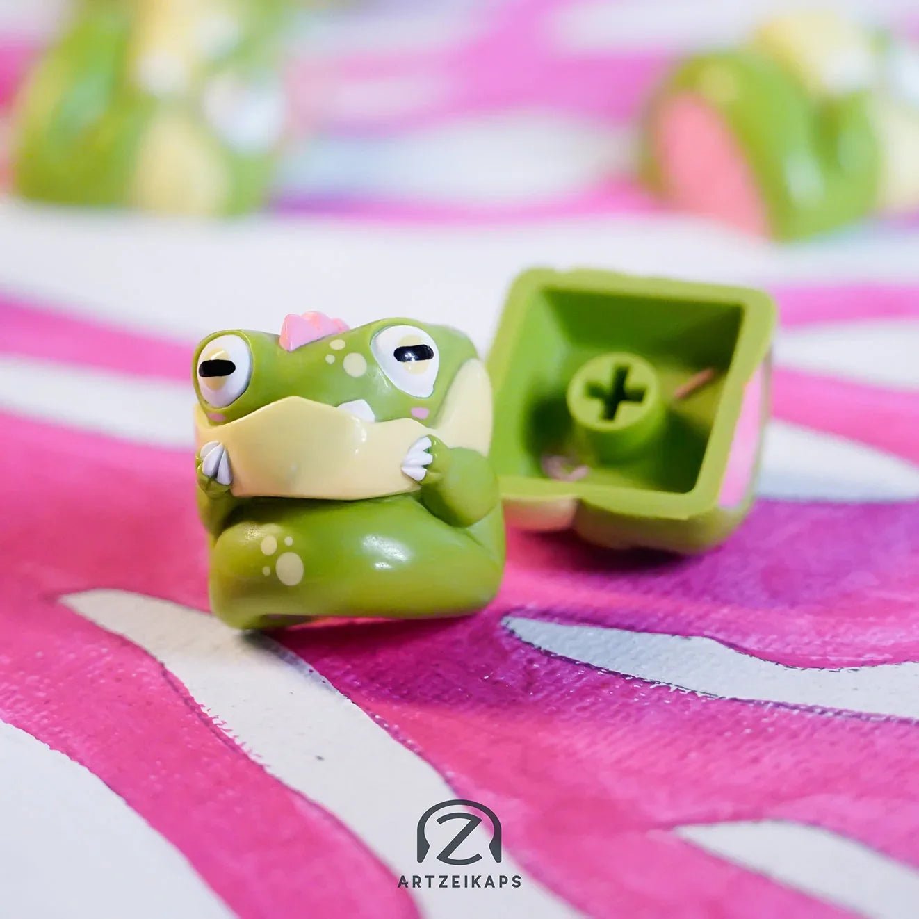 Chomper Kaeru artisan keycap in olive green frog design with front and back view on pink fabric background