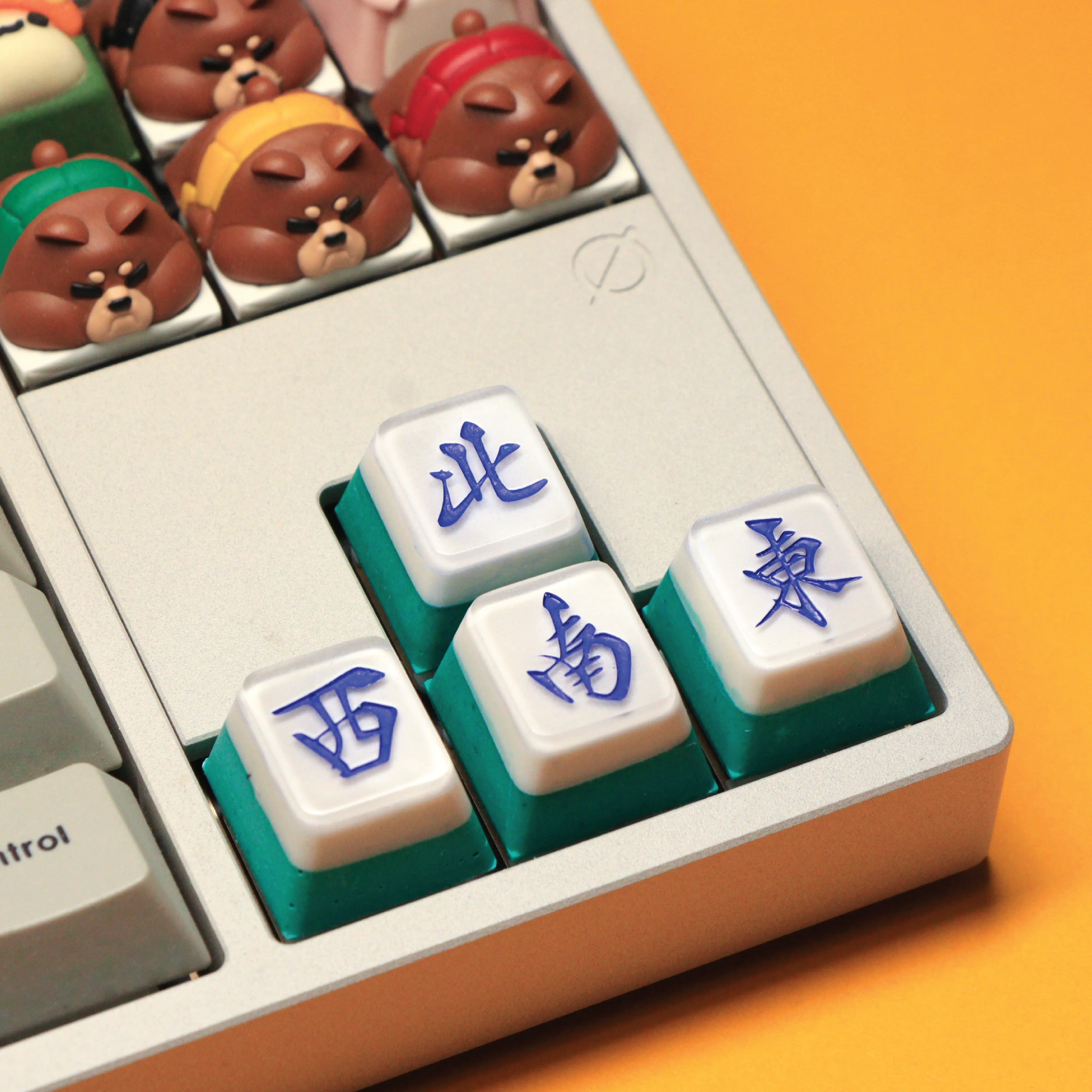 Mahjong Keycap Workshop Singapore. Close-up of a keyboard with custom keycaps featuring cartoon bears and Chinese characters on an orange background.