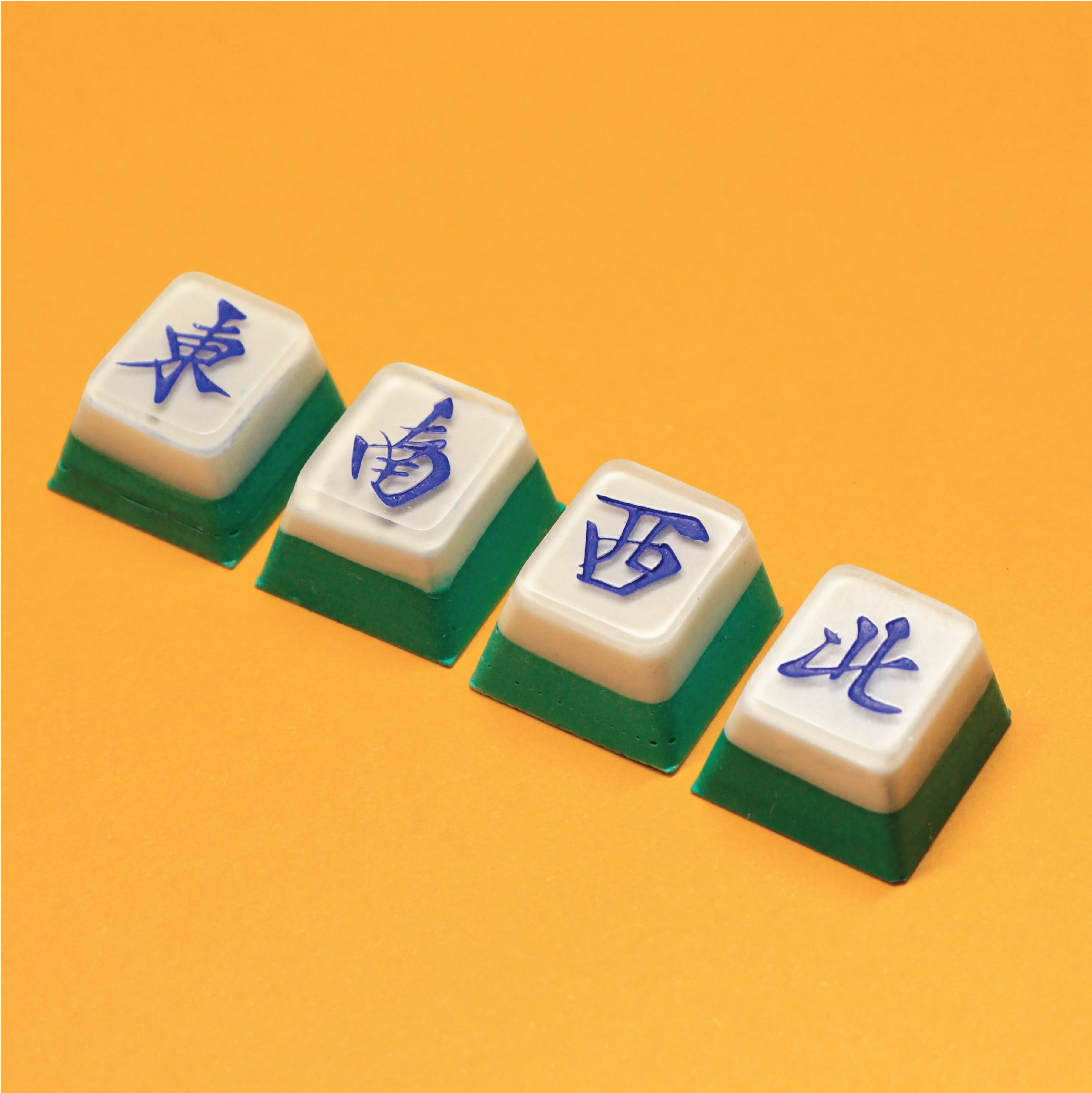 Mahjong wind tiles artisan keycaps (East, South, West, North) for mechanical keyboards on a bright yellow background.