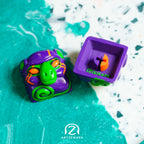 Smunkey GMK M-01 artisan keycap in purple with neon green and orange details, front and back view on teal terrazzo surface