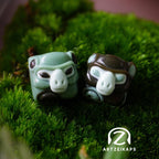 Smunkey GMK November Fog artisan keycap pair in dark brown and sage green, side angle view on moss