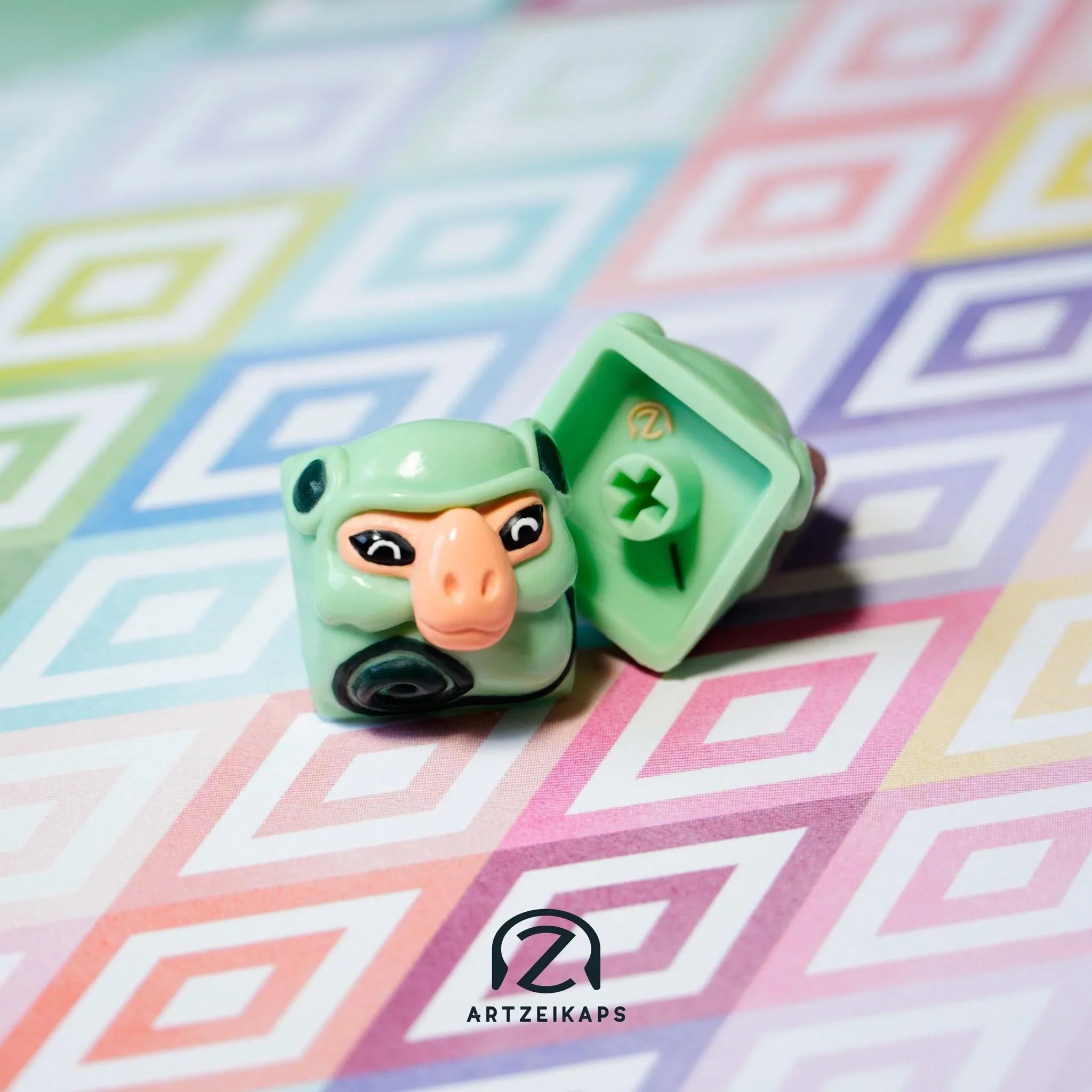 Smunkey Minty Peach artisan keycap in mint green with peach nose, front and back view on colourful geometric background