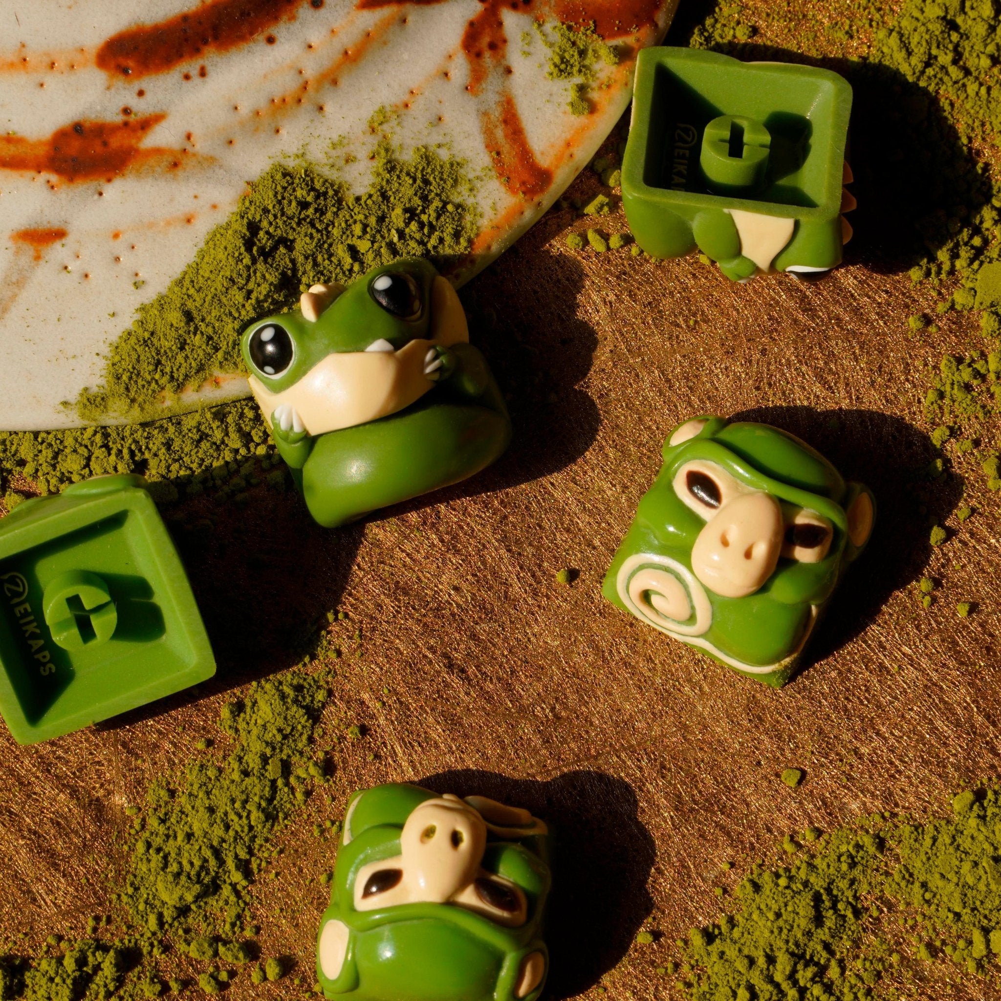 Chomper and Smunkey GMK Cream Matcha artisan keycap front and back view on matcha powder surface, top-down angle